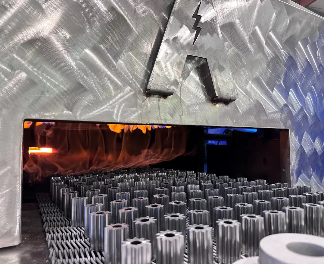 Powder metal gears on a mesh belt entering a Symmco sintering furnace